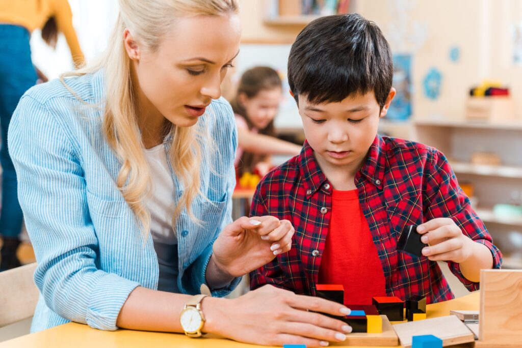 Selective focus of teacher and child playing building blocks with kids at background in montessori